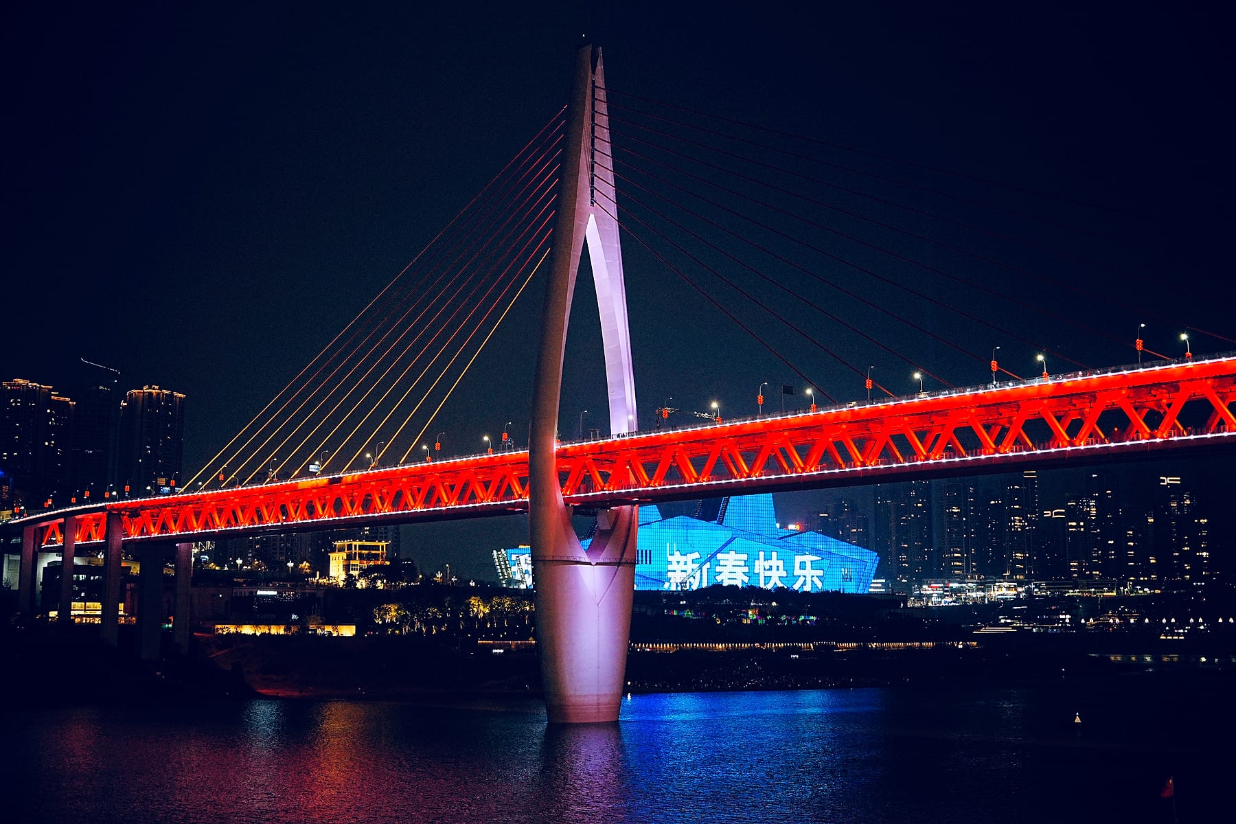 夜色中，红色桥梁与放射状桥索横跨江面